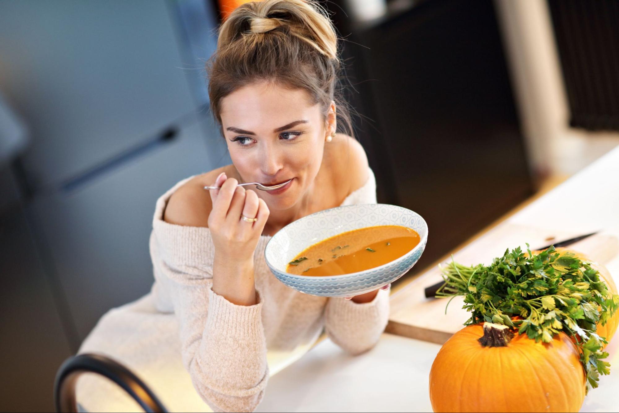 a woman eating pumpkin soup to represent What to Eat for Glowing Skin This Holiday Season