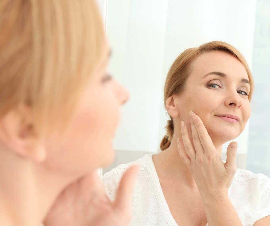 A middle aged woman looking at her skin in the mirror after a service to combat the signs of aging